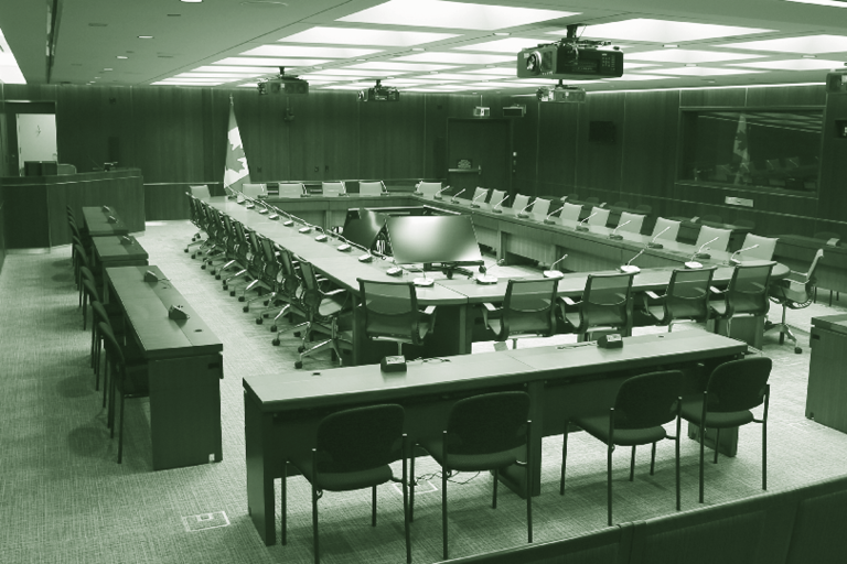 Photo d’une salle de comité typique, avec tables disposées en rectangle avec des fauteuils. Au-devant de la salle se trouve un gros podium pour l’agent de délibérations et vérification (l’opérateur de console).