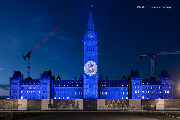 Édifice du Parlement illuminé en bleu royal avec le monogramme royal projeté sur la Tour de la Paix