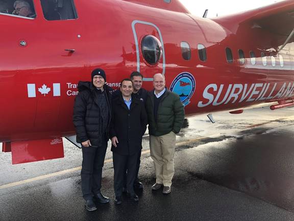 Photo de quelques membres du Comité des affaires étrangères se tenant devant un aéronef rouge Dash-7 de Transports Canada qui est utilisé dans le cadre du Programme national de surveillance aérienne. La photo a été prise sur l’aire de trafic de l’aéroport d’Iqaluit.