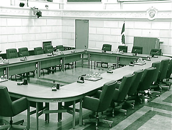 Photo d'une salle de comité typique, avec tables disposées en rectangle et entourées de fauteuils. Au devant de la salle se trouve un gros podium pour l'opérateur de console.